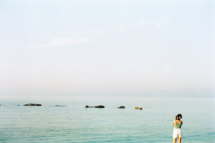 A person standing in a calm, pale sea, with rocks on the horizon