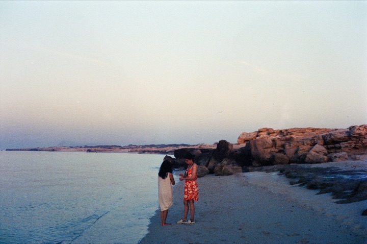 Two people at the water’s edge at dusk, beside a rocky shore