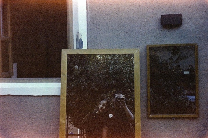 A self-portrait with a camera, reflected in a mirror leaning on a wall